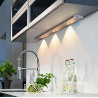 LumaBar Sensor 30 cm instalada bajo un mueble de cocina moderna, proyectando tres conos de luz calida sobre el muro y con el sensor de movimiento activo